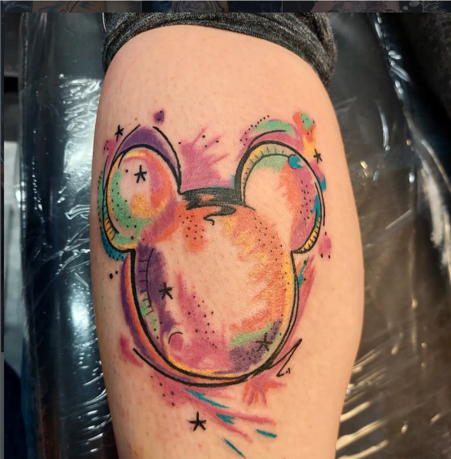 Colourful abstract mouse head tattoo with watercolour-style details on a thigh