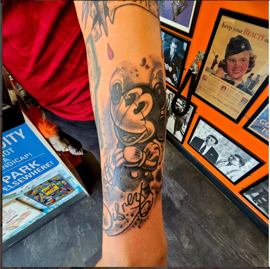 Black and grey cartoon bear tattoo with script lettering on a forearm