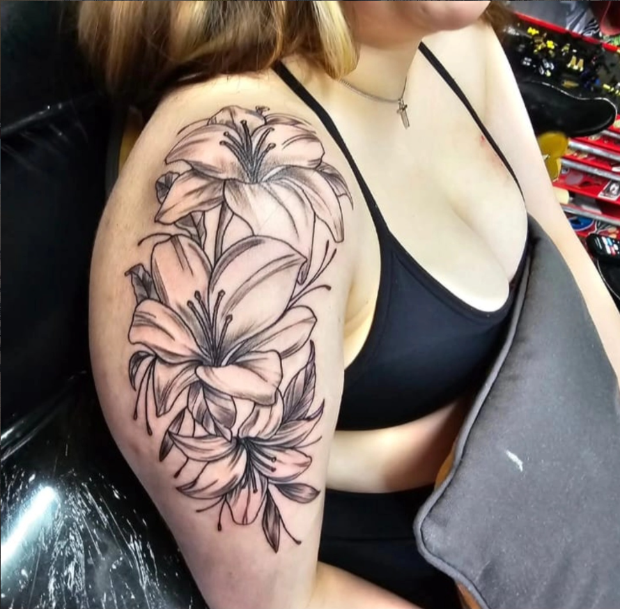 Black and grey lily flowers tattooed across the upper arm