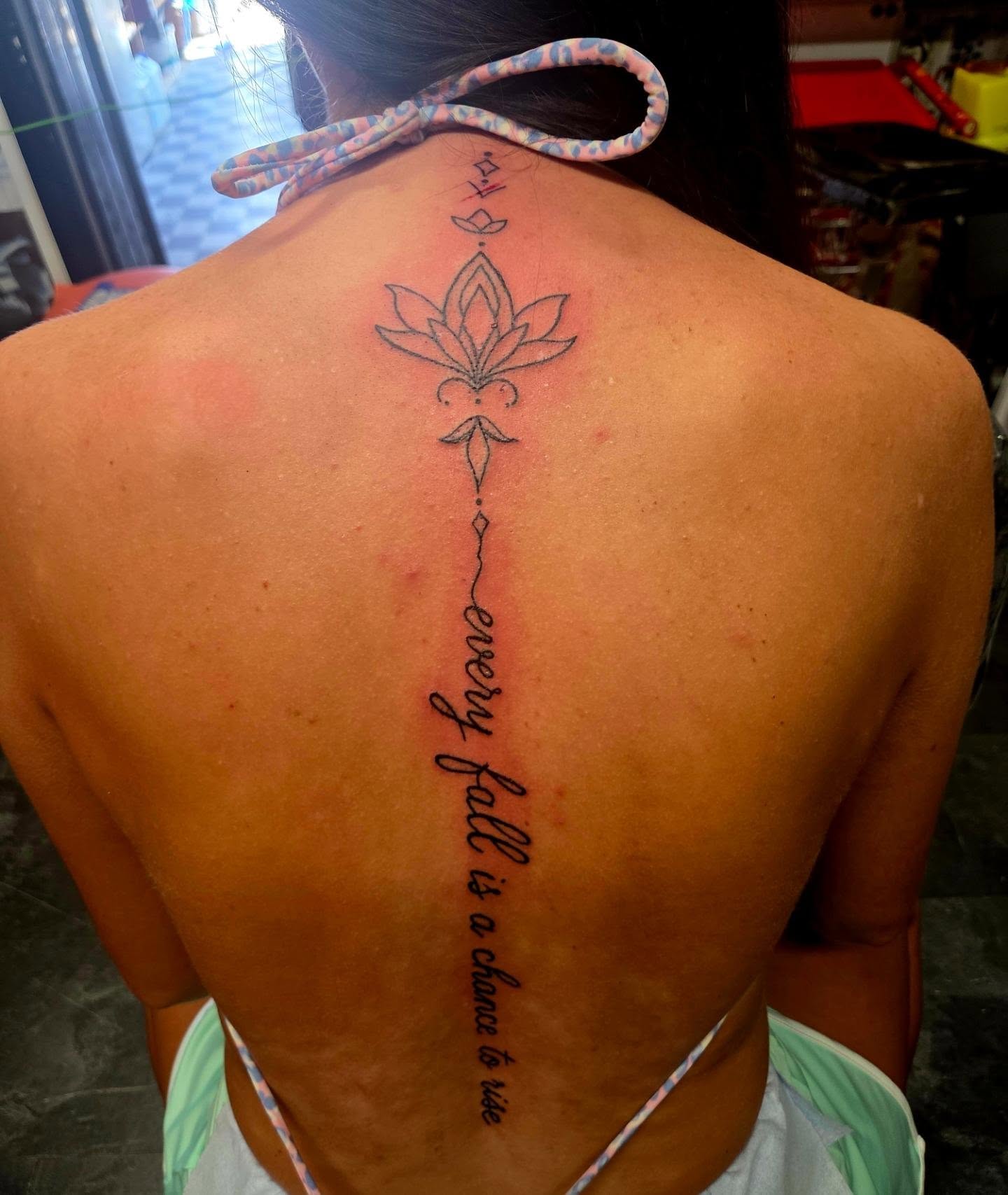 Fine-line lotus ornament and script lettering tattoo down the back