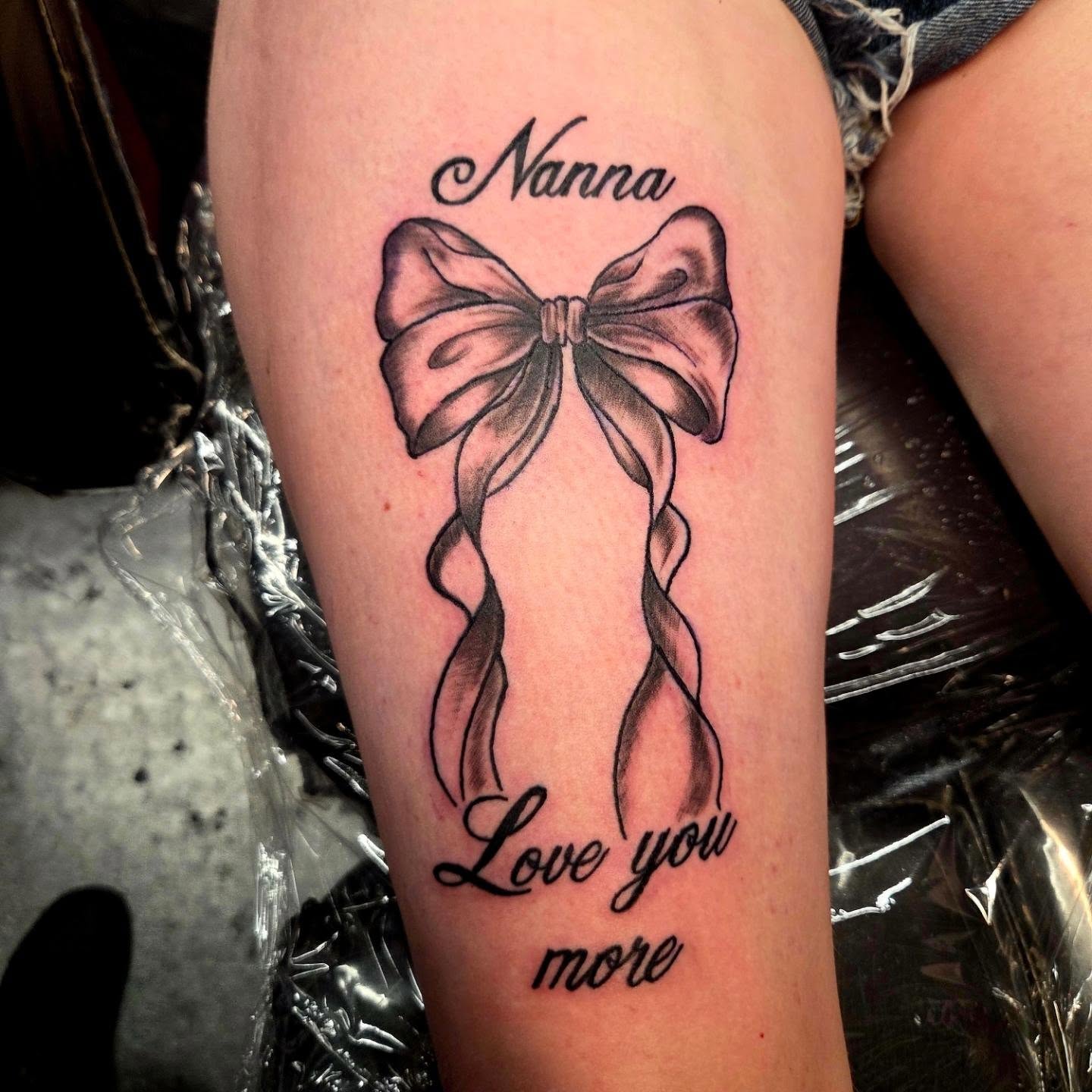 Memorial bow and Nanna lettering tattoo in black and grey on a thigh