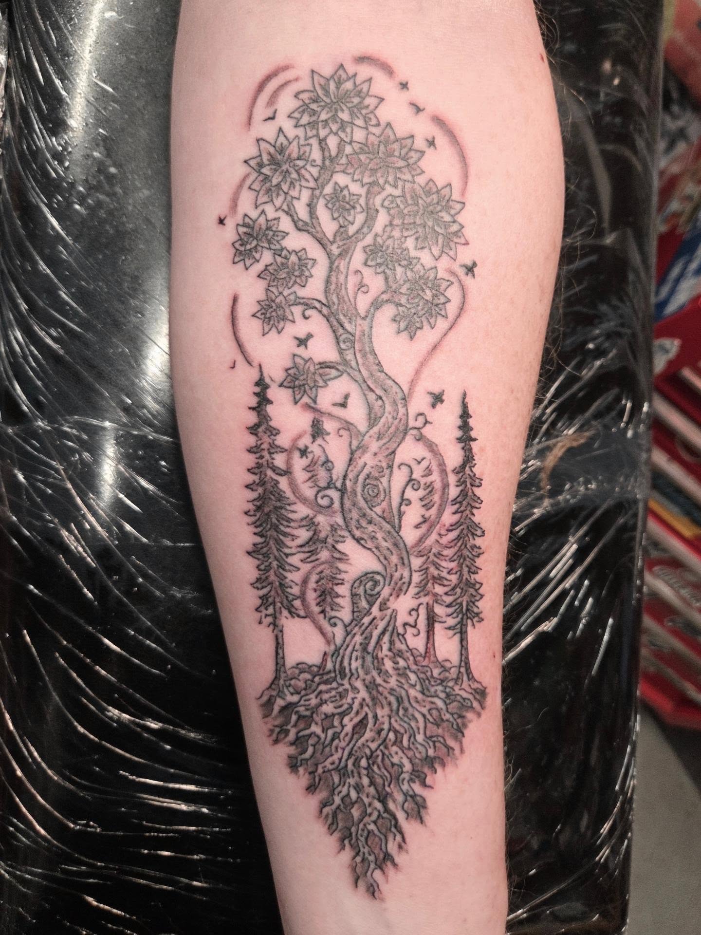 Detailed black and grey tree and woodland tattoo on a forearm