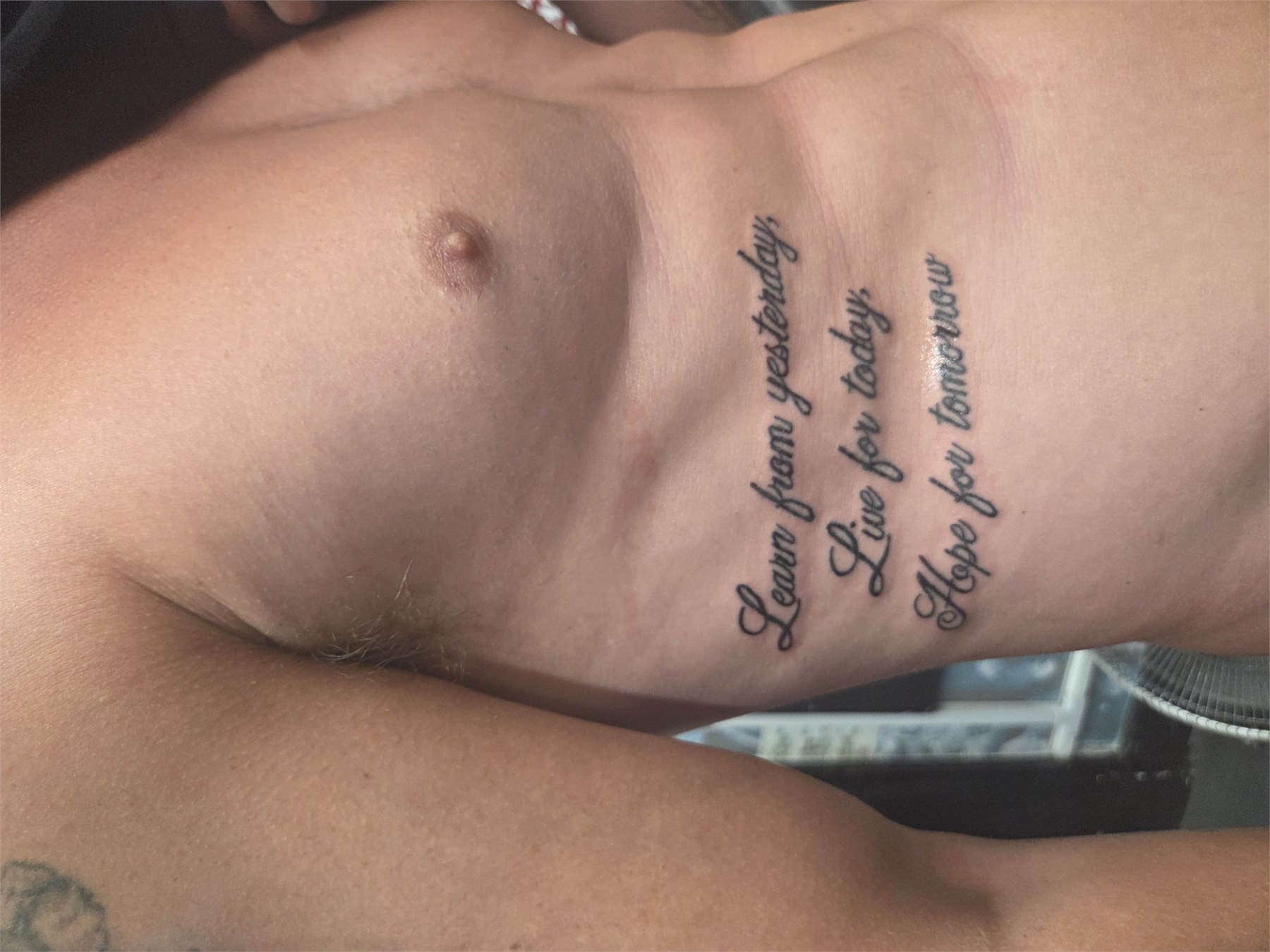 Fine script lettering tattoo along the ribs